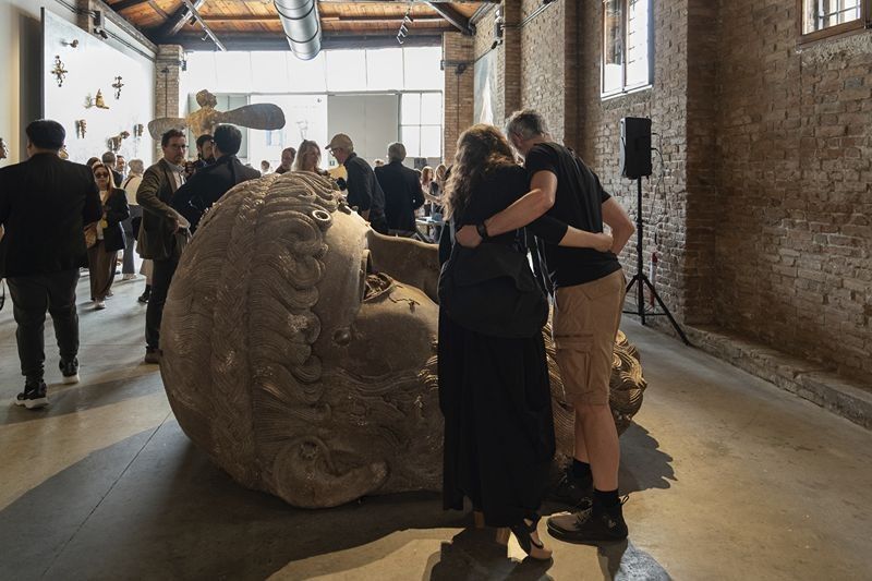 A couple embraces beside a giant carved reclining head during the LUNA opening in a brick-walled hall