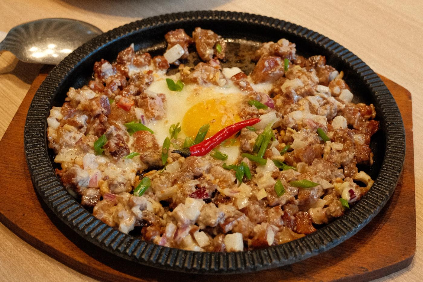 Paboritong Sisig sizzling on a cast iron plate, topped with an egg yolk and a red chili