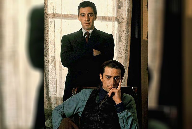 Al Pacino stands arms crossed behind a seated young Robert De Niro in a Godfather Part II publicity shot