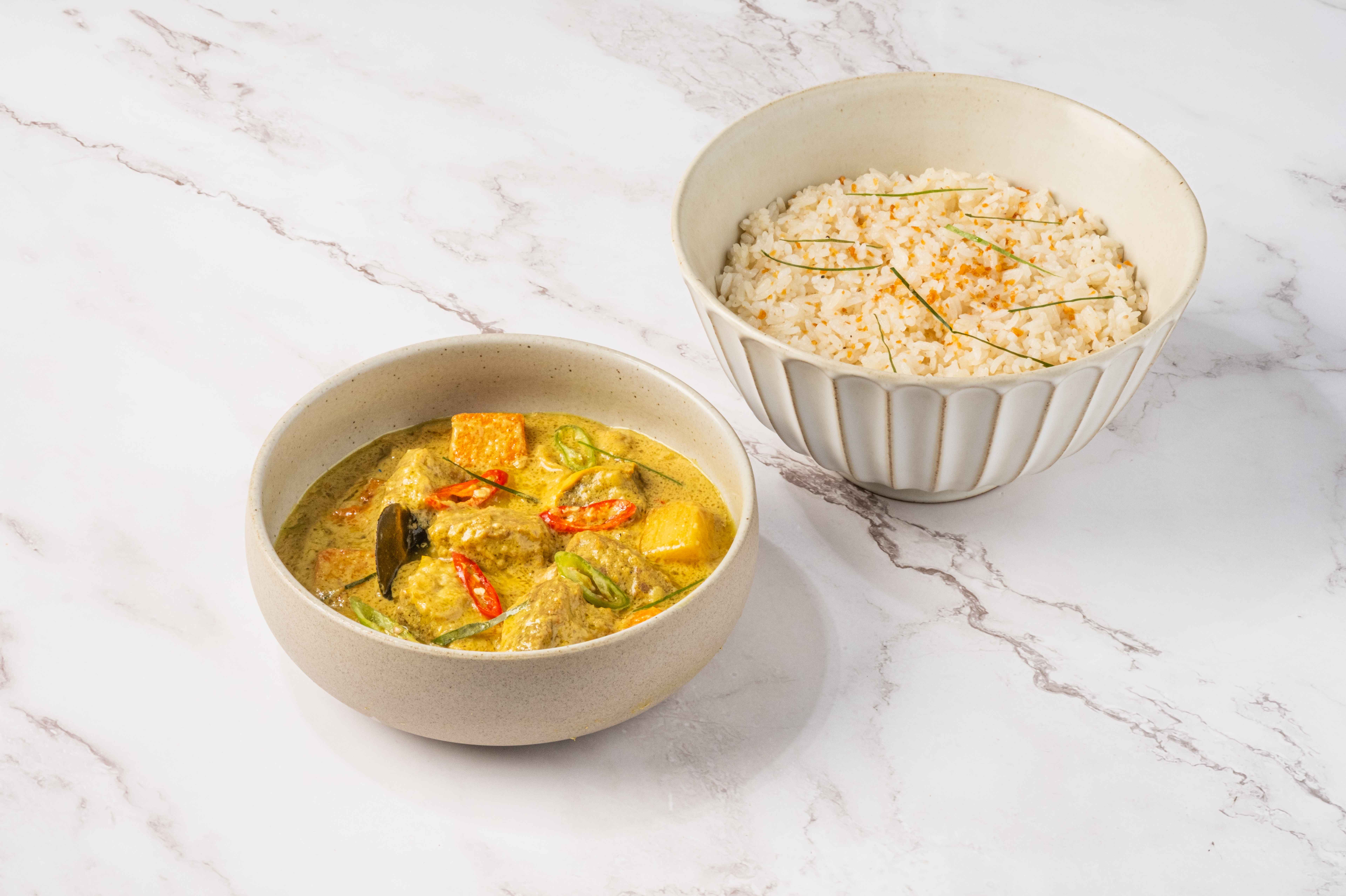 Beef rendang in a pale coconut curry with red chili and vegetables, served beside a bowl of steamed rice