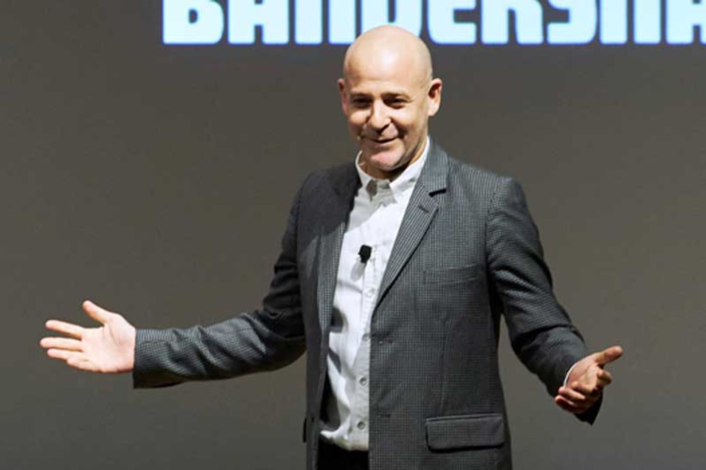 Peter Friedlander spreads his arms onstage in front of a giant Bandersnatch title screen