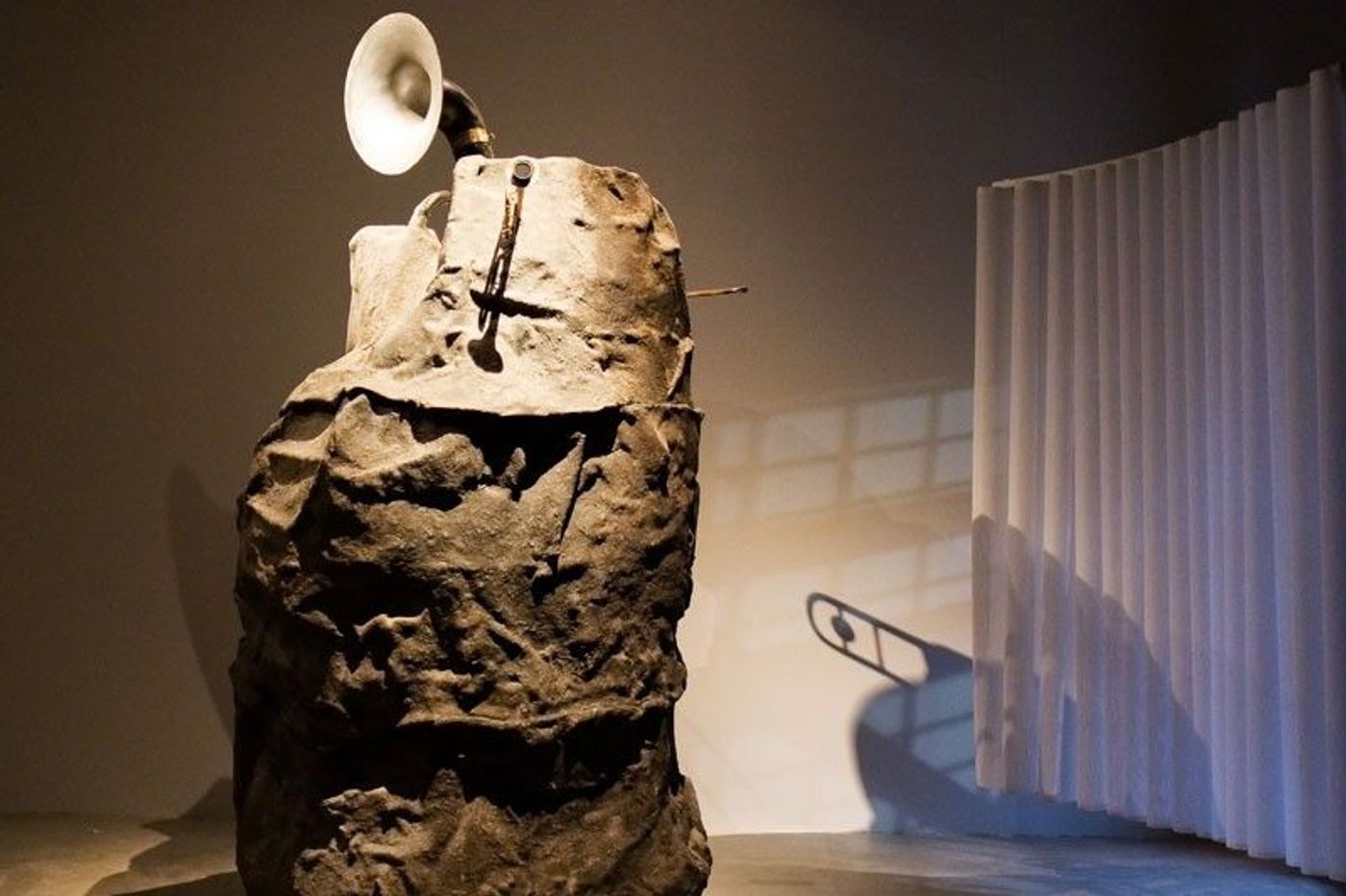 A boulder sculpture sprouting a brass horn and trumpet, part of Mark Salvatus’s Pavilion installation