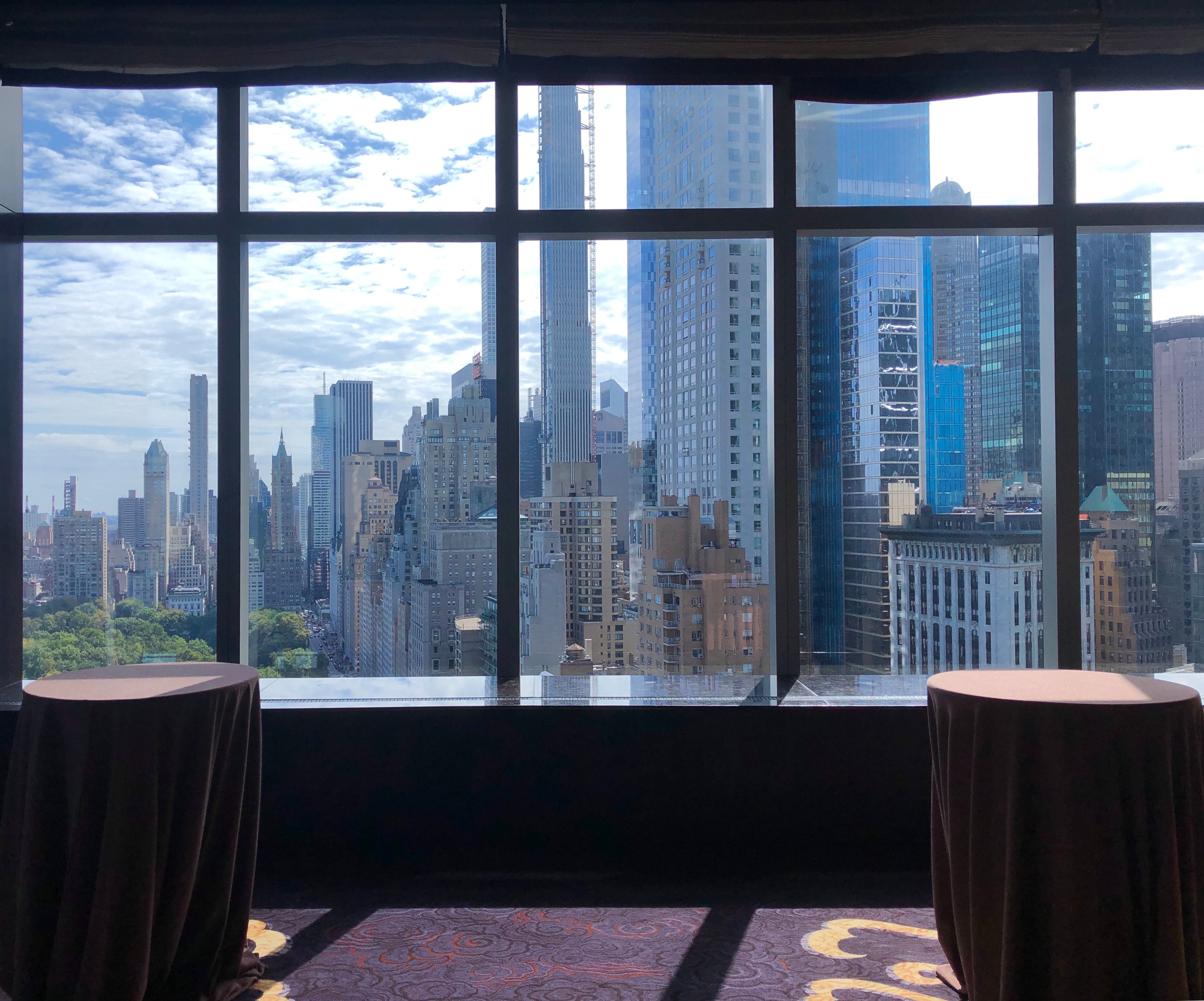 Midtown Manhattan skyline and the edge of Central Park seen through tall windows behind draped cocktail tables