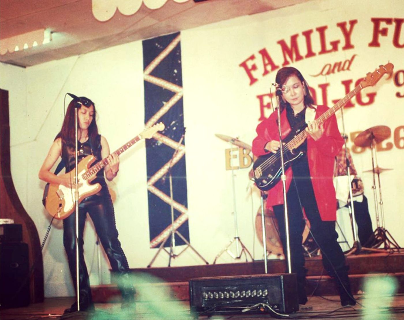 An old photograph of a young Barbie Almalbis playing electric guitar onstage beside her mother on bass, under a hand-painted Family Fun banner