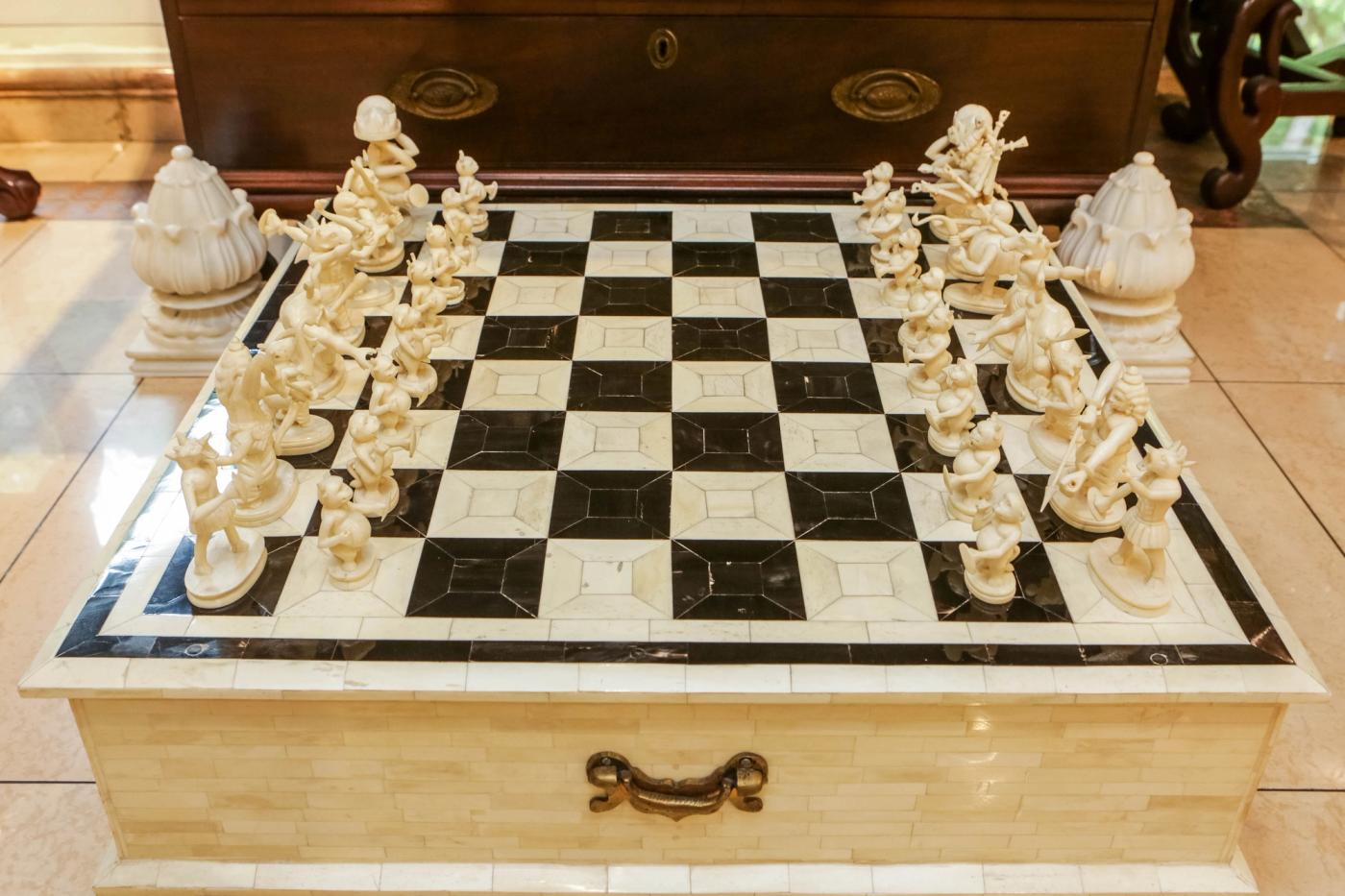 A chess set of carved white figures on a black-and-white marble board resting on an inlaid bone chest