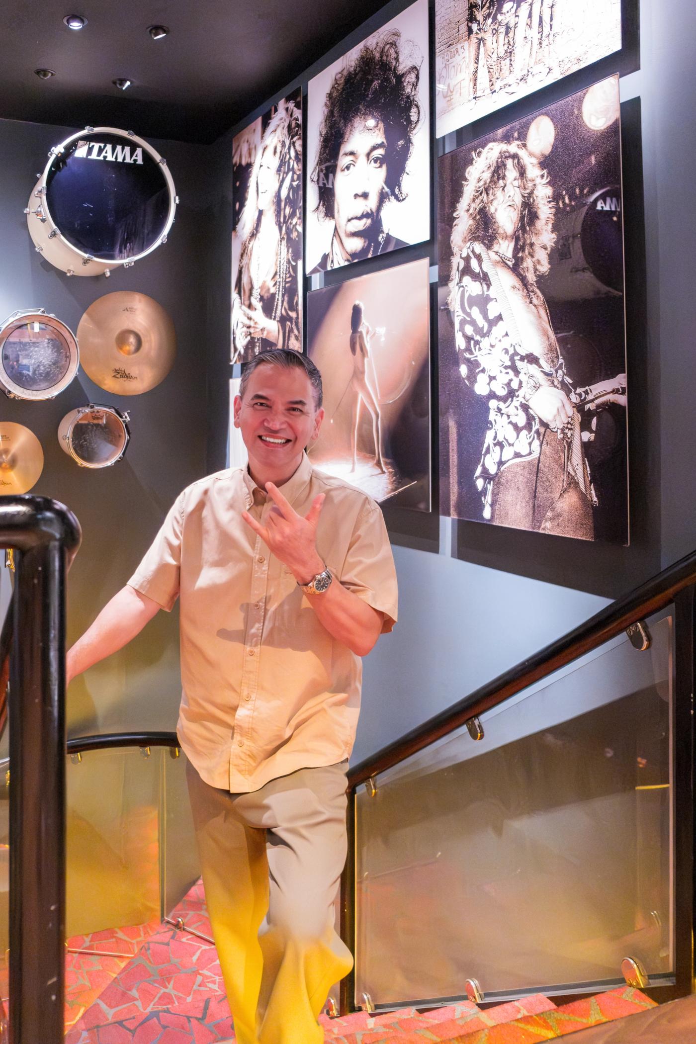 Jean Paul Manuud flashes a rock sign on a staircase lined with cymbals, drums and rock star portraits