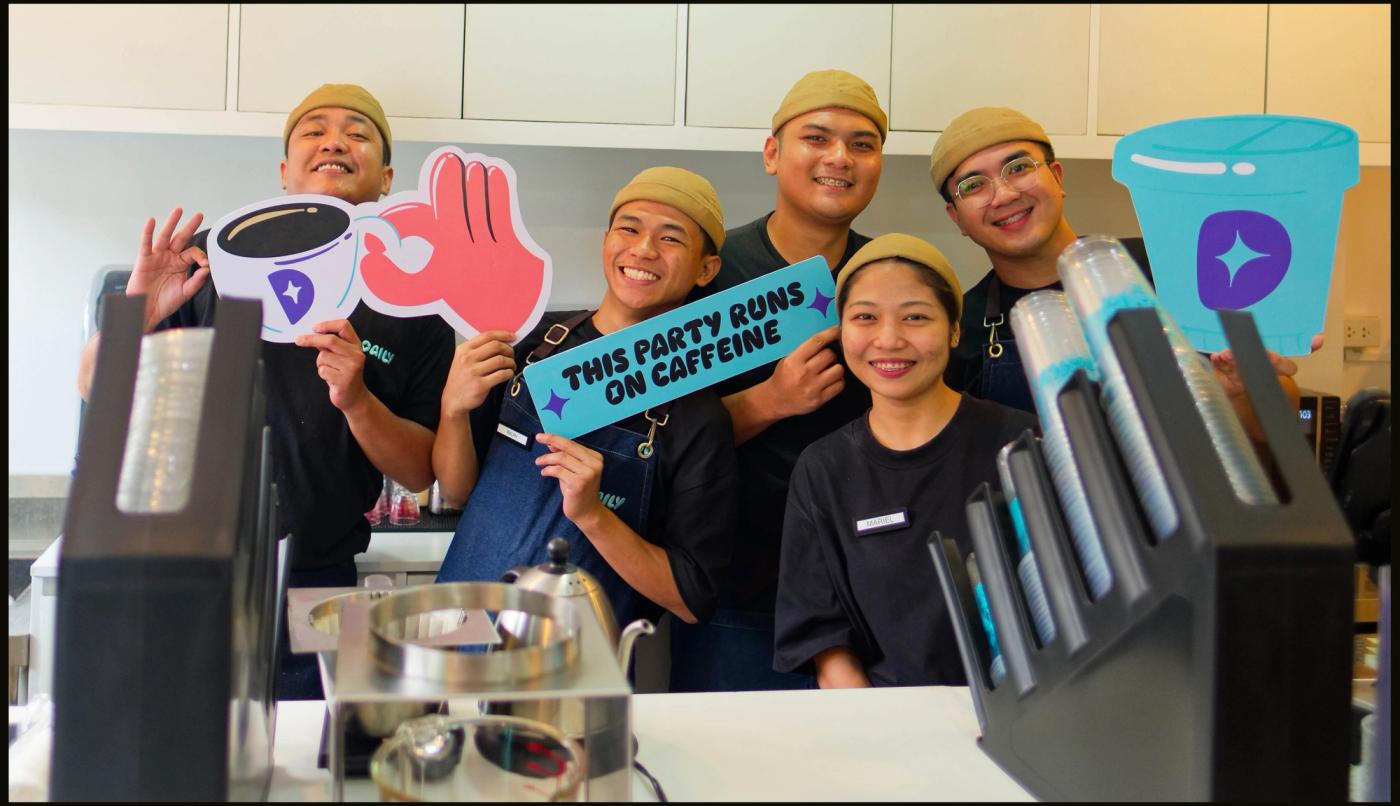 Five Daily by Bo’s Coffee staff in tan caps grin behind the counter holding coffee-cup cutouts and a ‘This party runs on caffeine’ sign