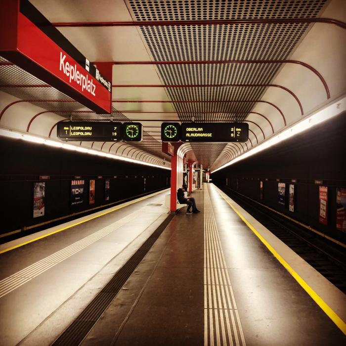 Deserted Keplerplatz U-Bahn platform in Vienna with red signage and a lone figure on a bench