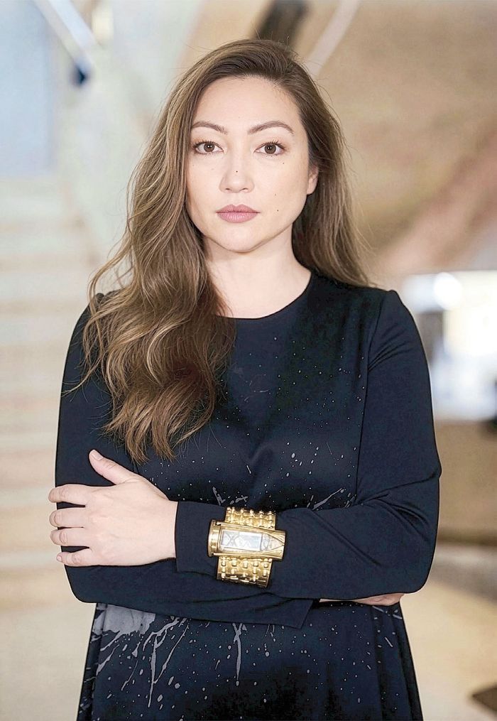 Michelline Syjuco in a black long-sleeved top, arms crossed, wearing a gold and crystal statement cuff