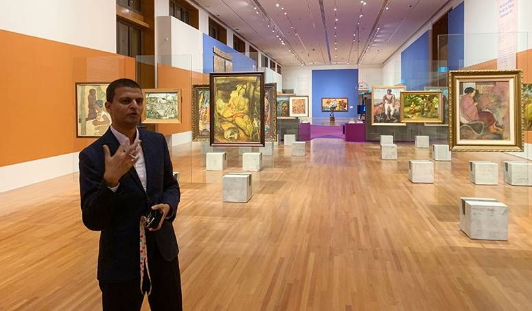 Senior curator Shabbir Hussain Mustafa gestures mid-tour in a gallery of gold-framed paintings
