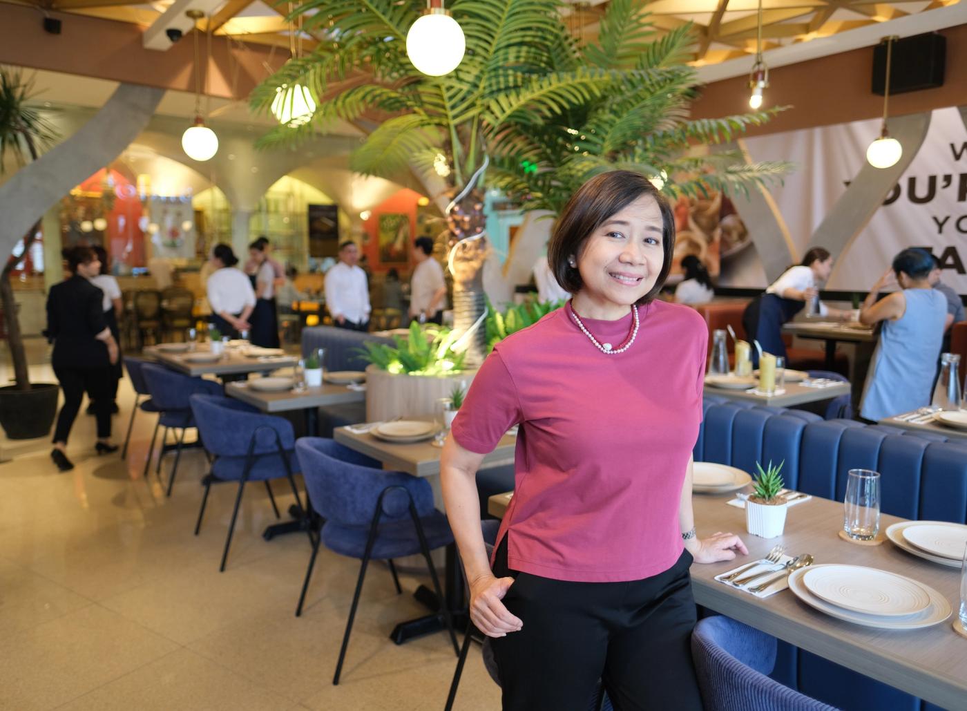 Lisa Ronquillo-Along stands beside plated tables and blue banquettes in the bright dining room
