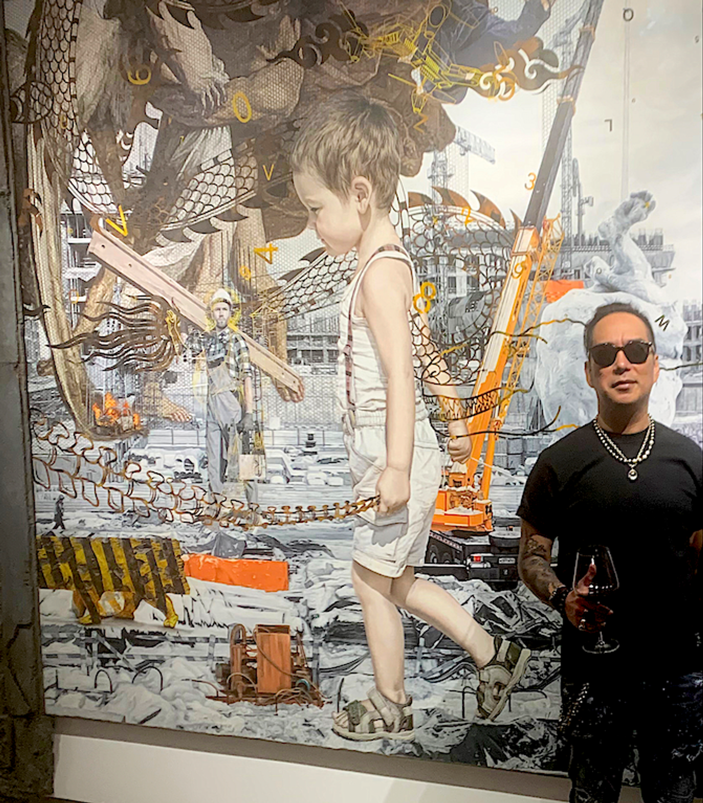 Ronald Ventura, wine glass in hand, beside his ‘Kalupaan’ painting of a child walking through a construction site
