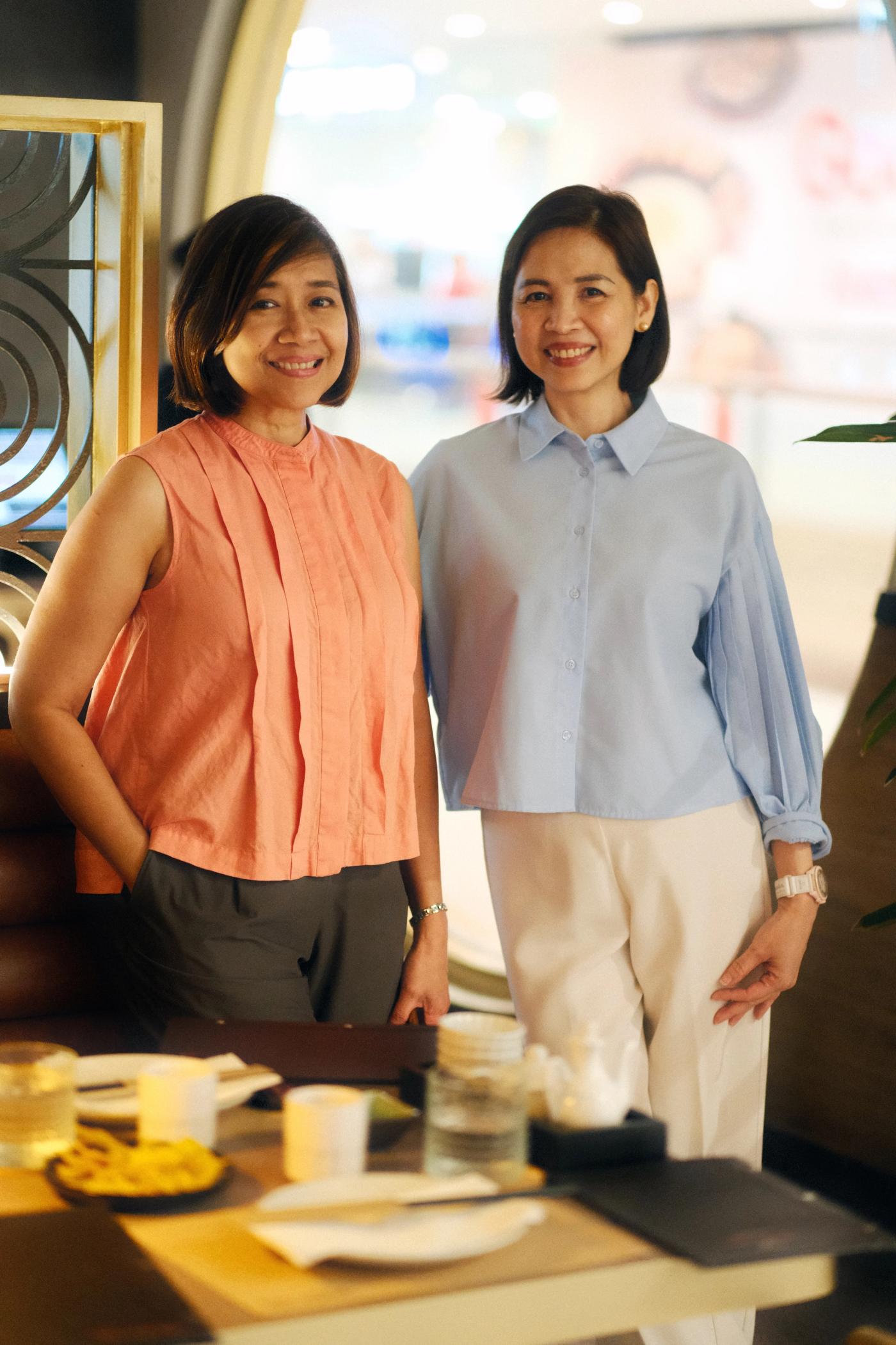 The Bistro Group executives Lisa Ronquillo-Along and Divine Peralta smiling in front of a brightly lit modern restaurant interior