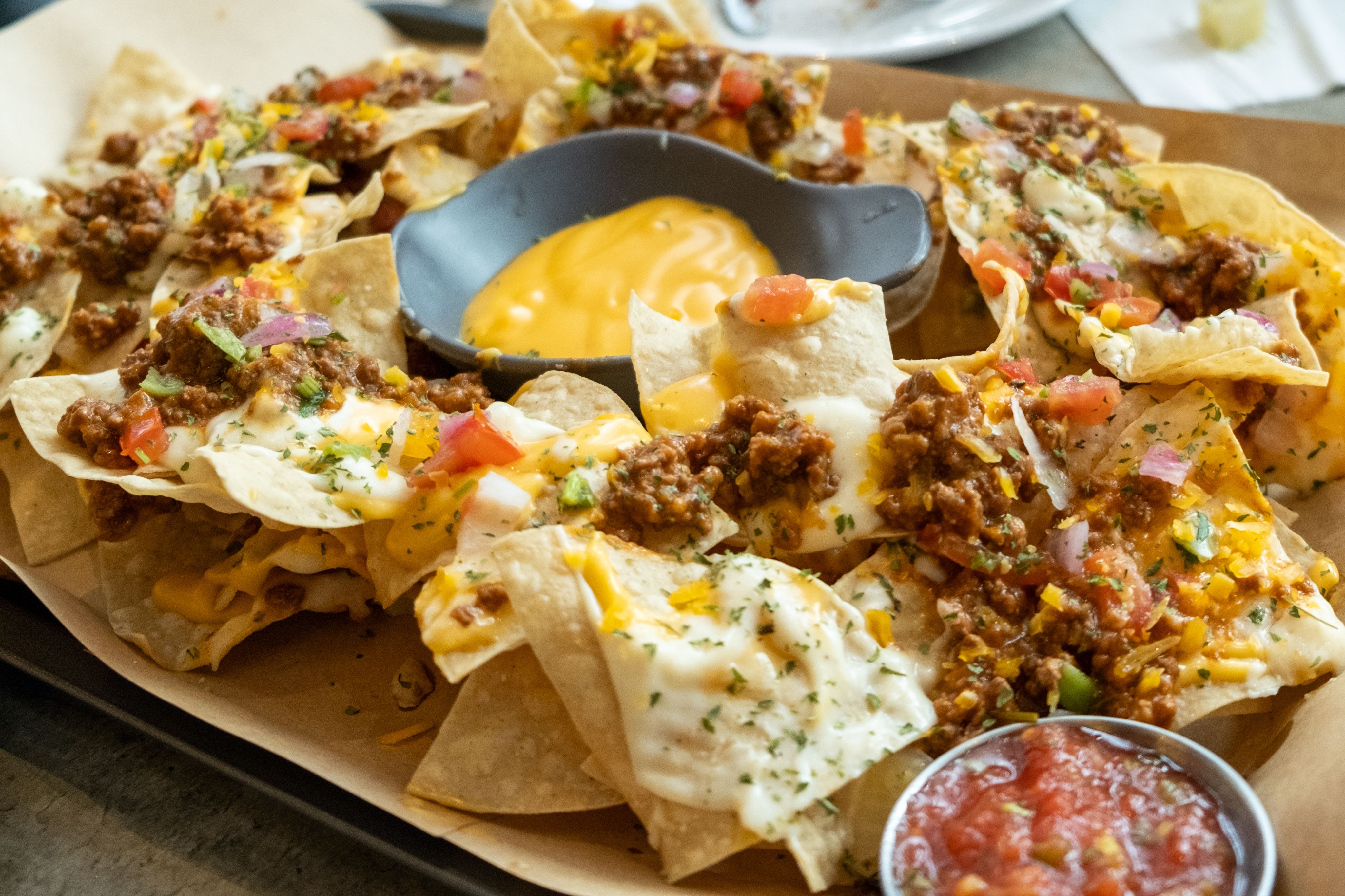 Loaded nachos piled with ground beef, melted cheese and tomato around a pot of cheese dip