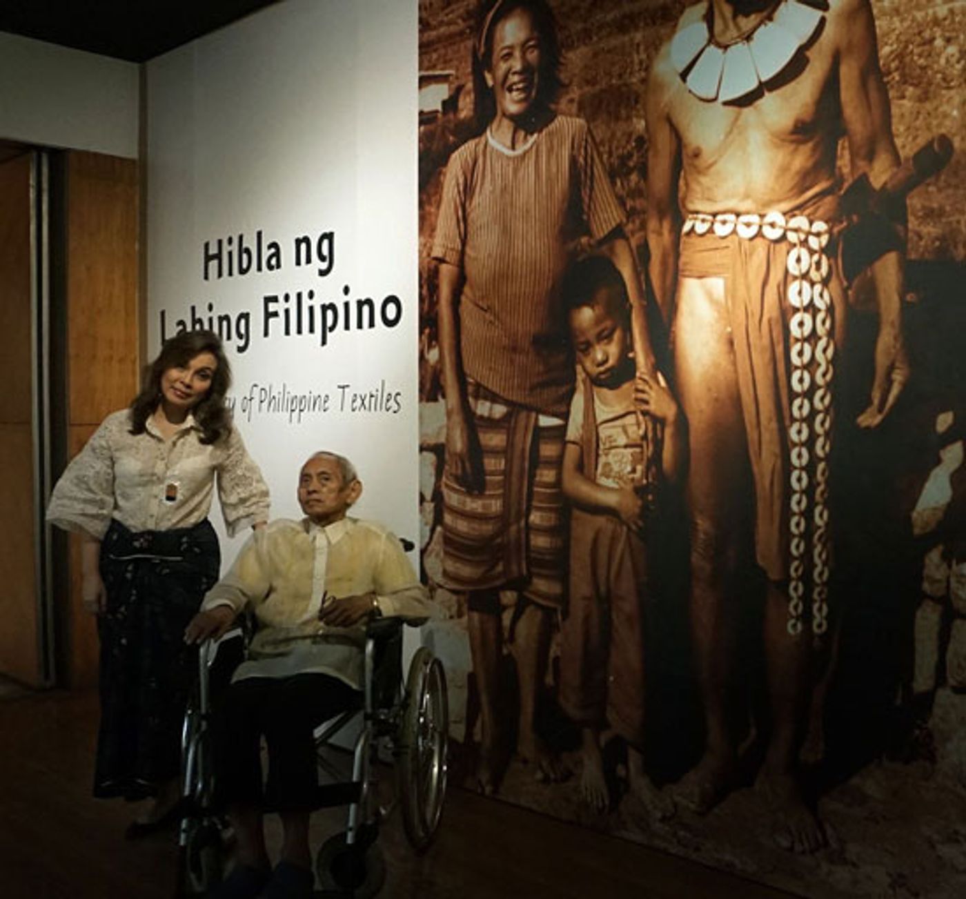 Loren Legarda standing beside David Medalla in his wheelchair at the Hibla ng Lahing Filipino textile gallery