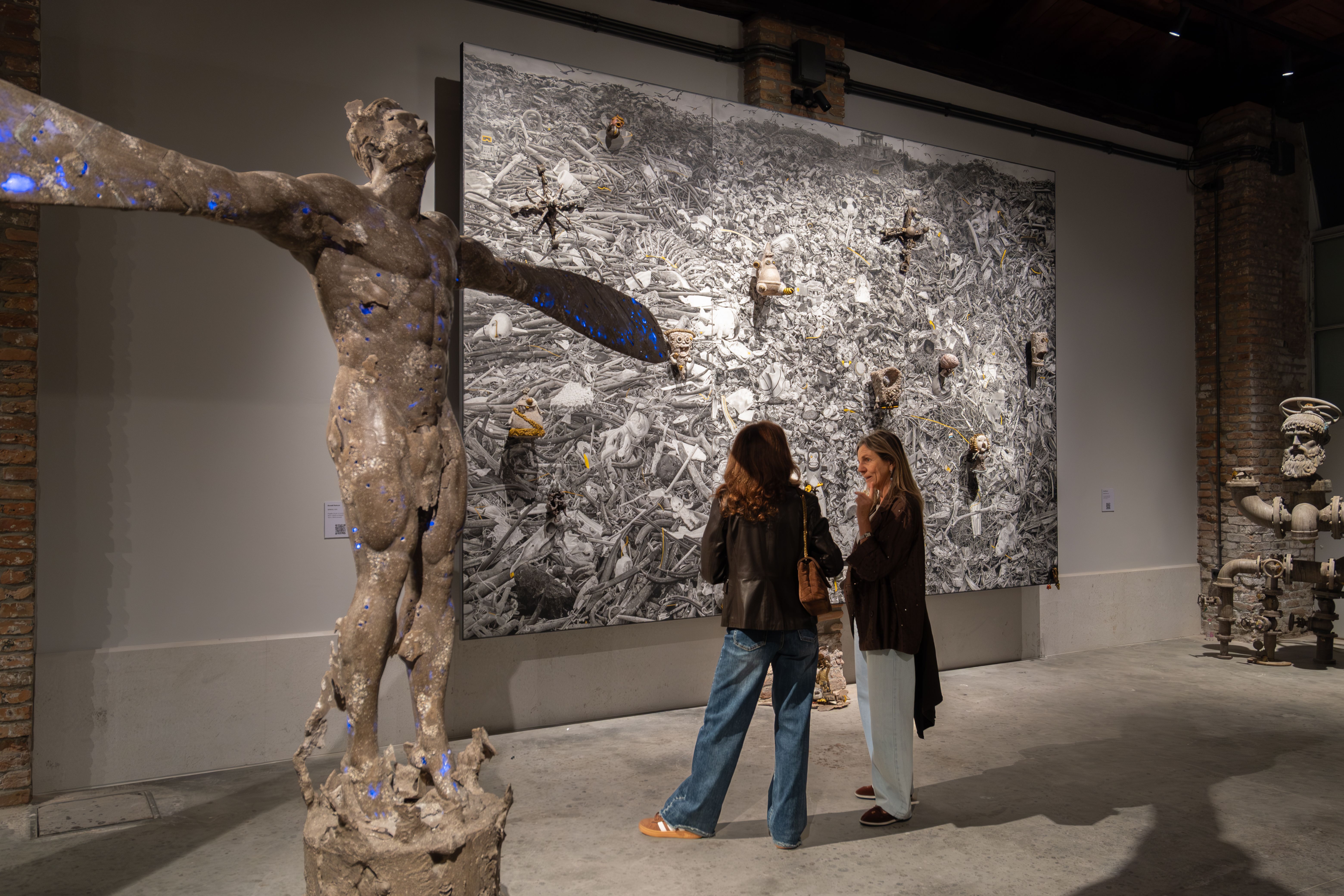 Visitors view a vast monochrome canvas behind a weathered winged figure sculpture in Ronald Ventura’s LUNA