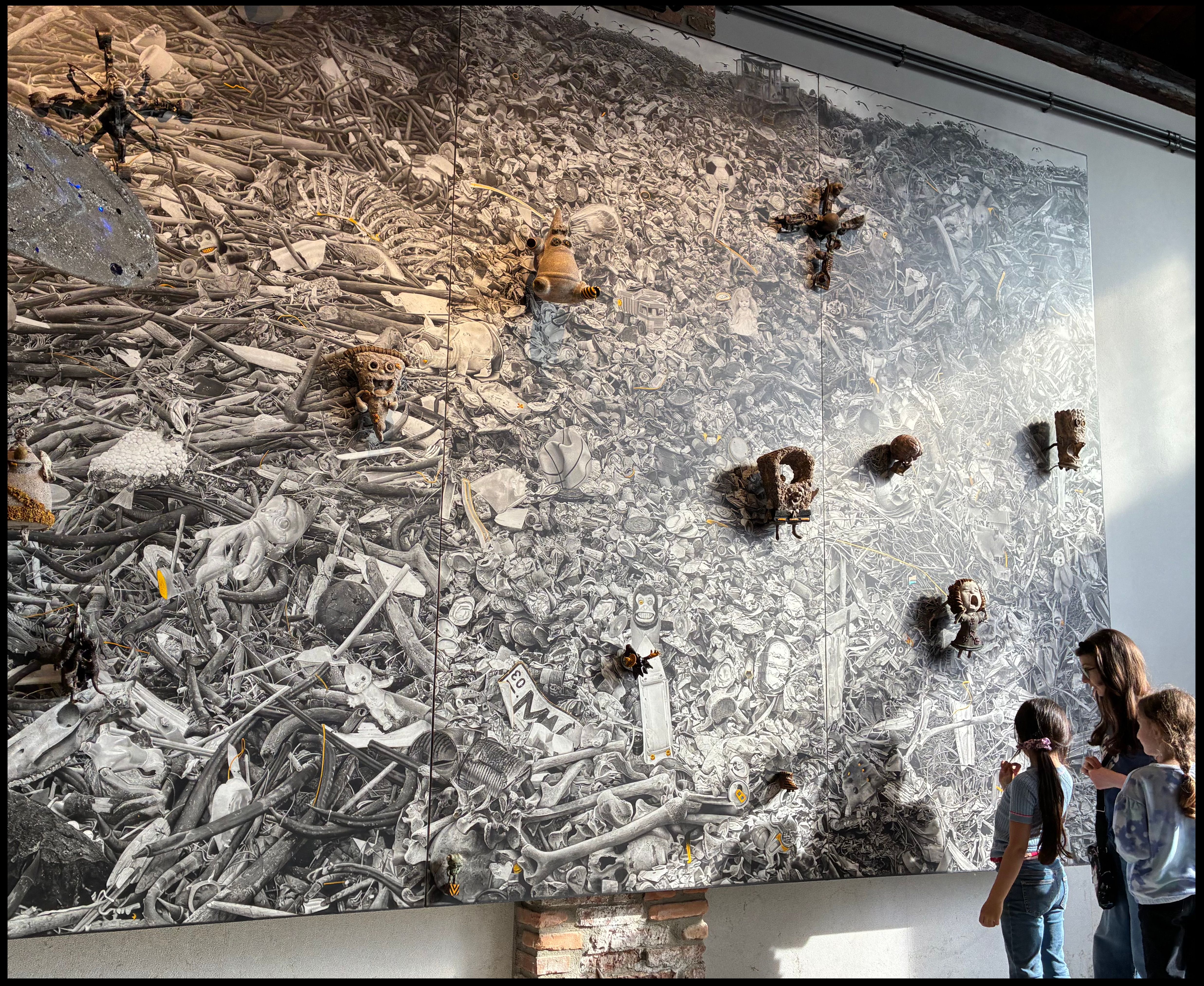 Visitors gaze up at the towering “Detritus” triptych, a wall-sized graphite field of drawn rubble, bones and relief objects, in the dock hall