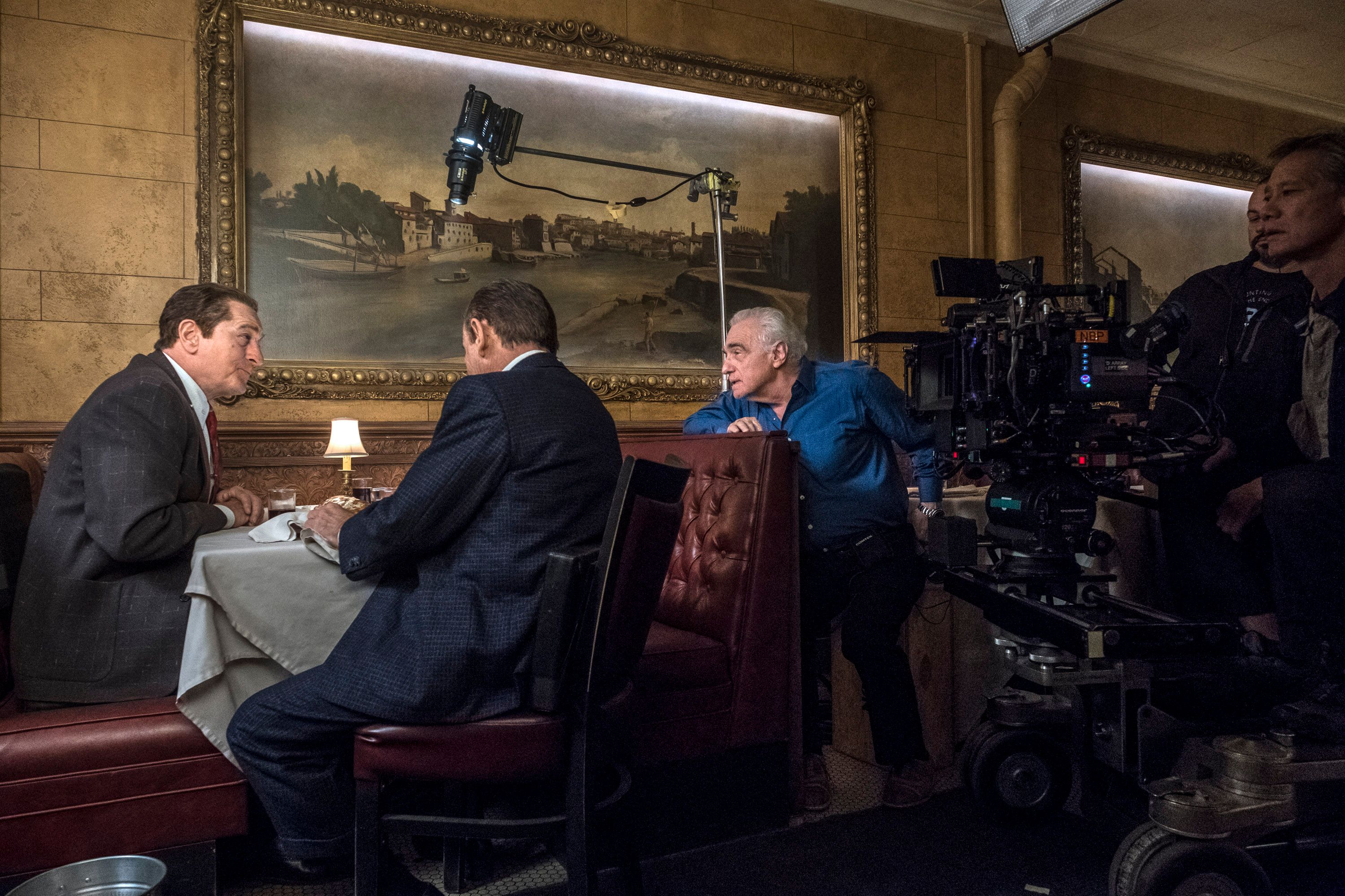 Martin Scorsese crouches beside the camera rig directing a dinner scene in a paneled restaurant