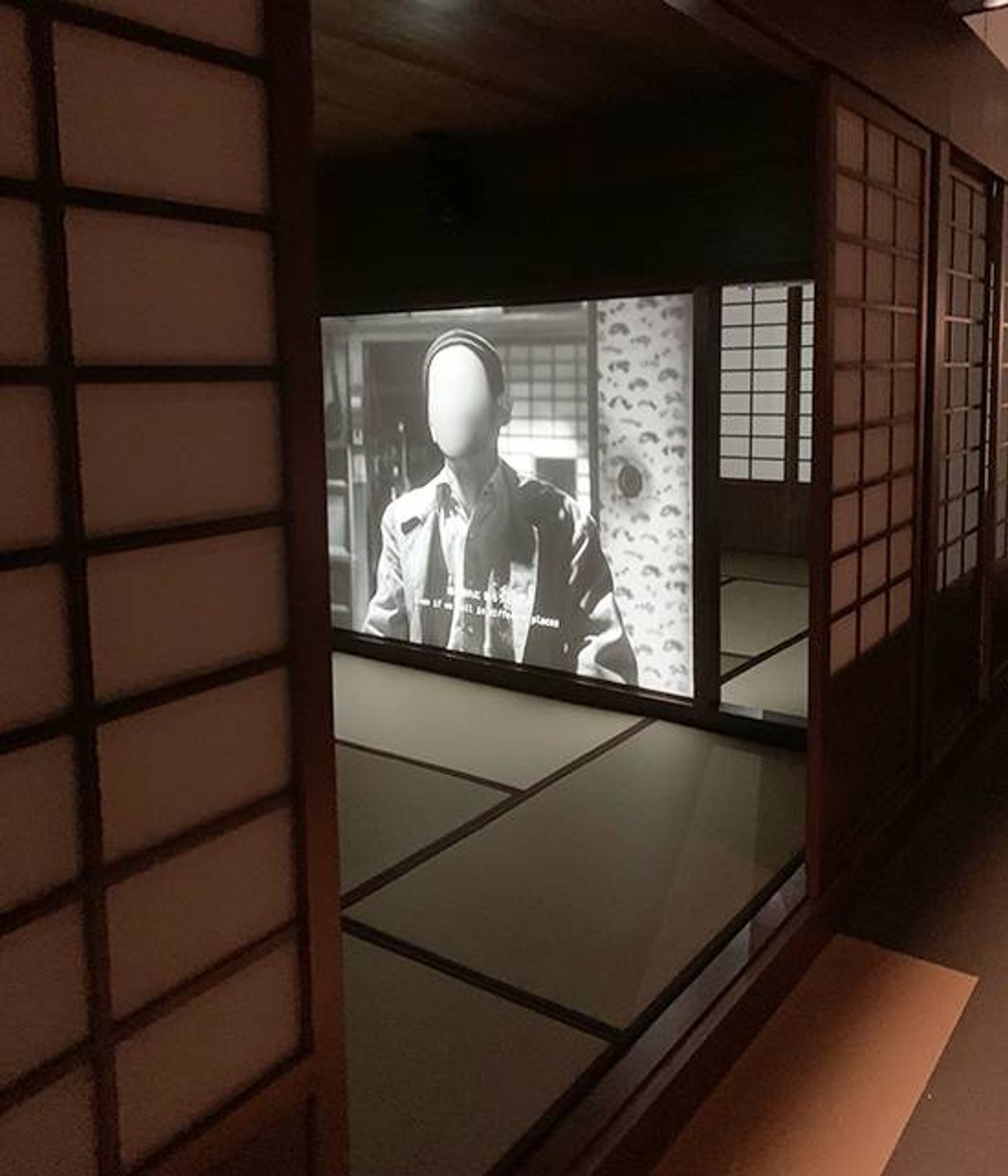 Black and white projection of a suited figure with a blank face, seen through shoji doors in Hotel Aporia