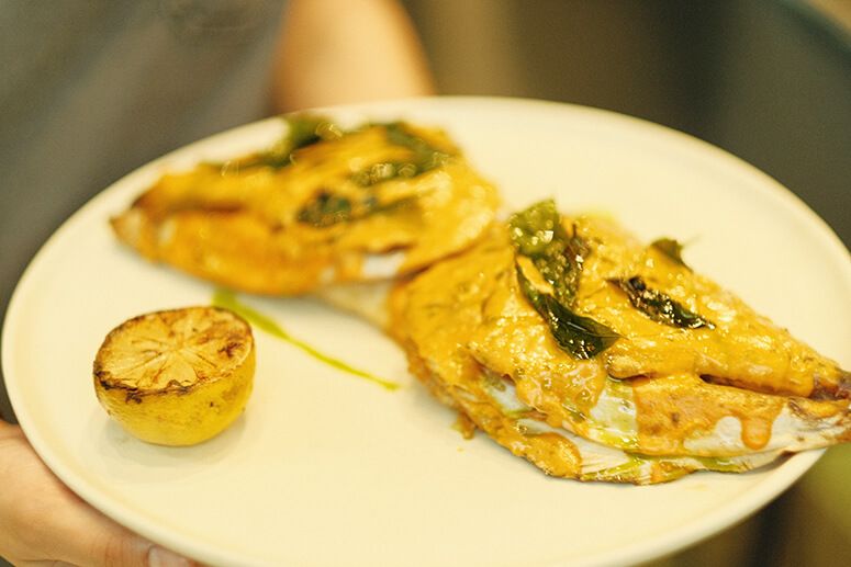 Salmon head halves coated in golden curry lemon sauce, served with a charred lemon on a white plate