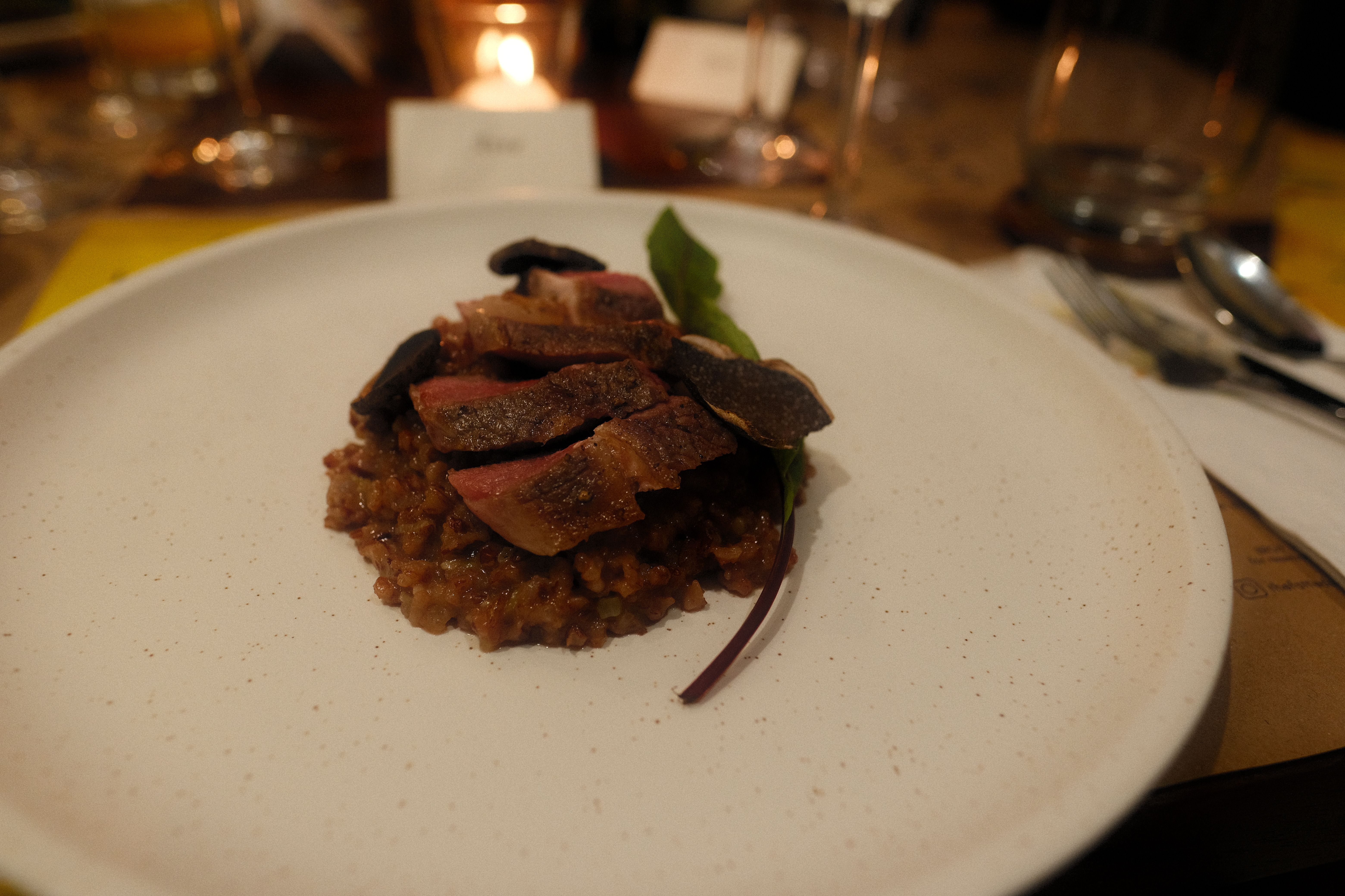 Arroz meloso topped with sliced seared duck and shaved black truffle on a white plate