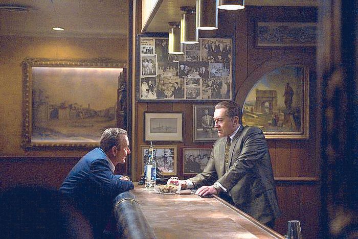 Joe Pesci and Robert De Niro talk across a dimly lit wooden bar lined with framed photographs