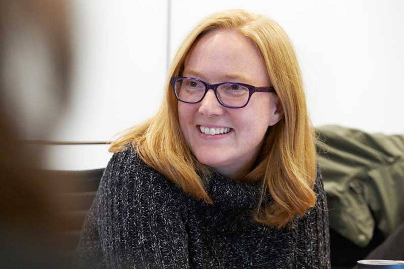 Netflix’s Carla Engelbrecht smiling in dark-rimmed glasses and a grey knit sweater