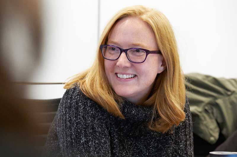 Netflix’s Carla Engelbrecht smiling in dark-rimmed glasses and a grey knit sweater