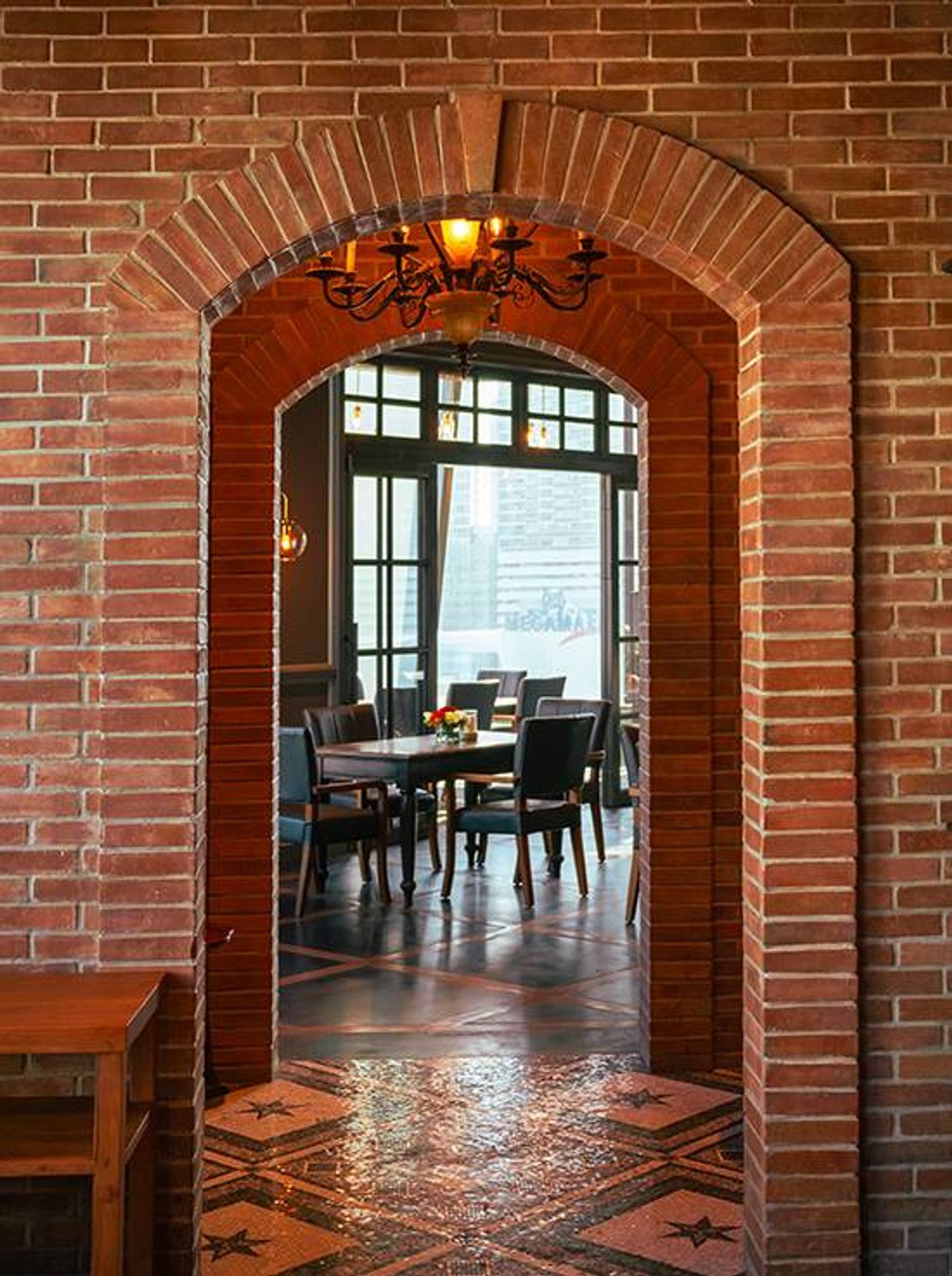 Brick archway at Osteria Antica framing a warm dining room with a wrought-iron chandelier and star-patterned mosaic tile floor