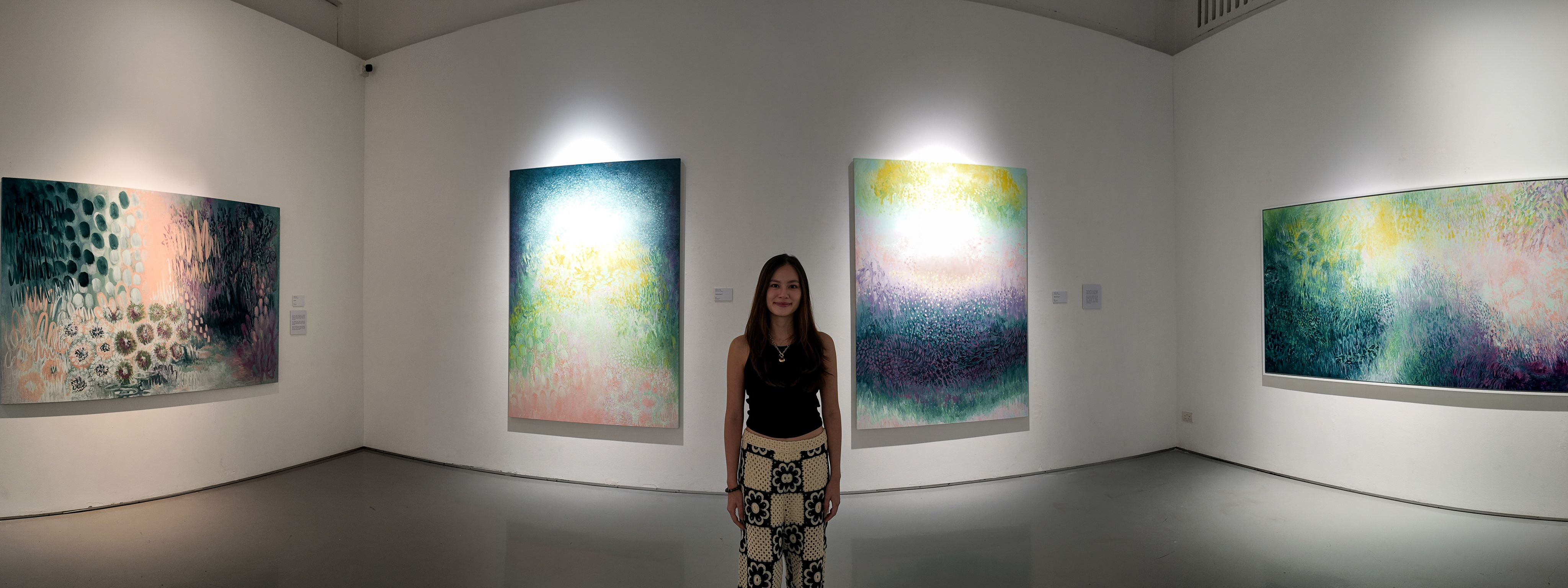 Maria Tan at the center of her First Light exhibition, four glowing abstract canvases around her at The Columns Gallery