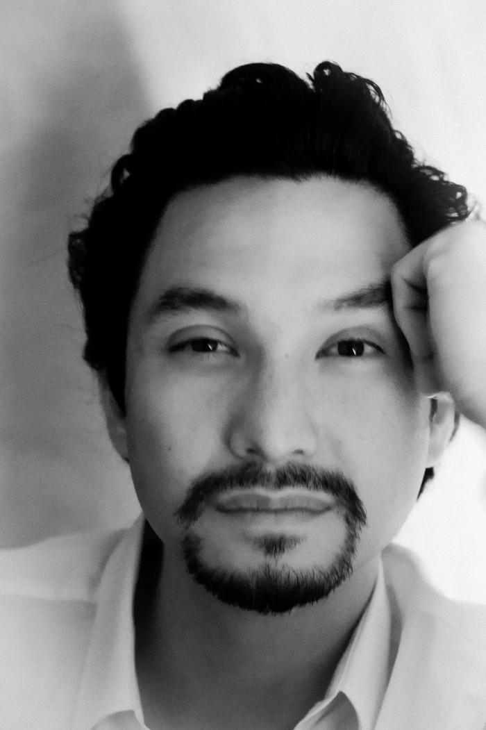 Portrait of Filipino author Miguel Syjuco leaning against a wall and looking at the camera