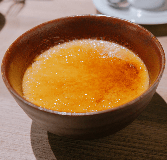 Crème brûlée with a caramelized amber surface served in a rustic brown ceramic bowl