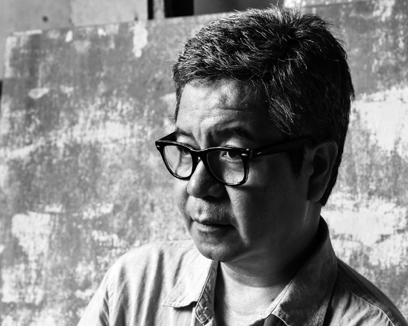 Black-and-white portrait of Gerry Tan in glasses, looking to one side against a weathered wall