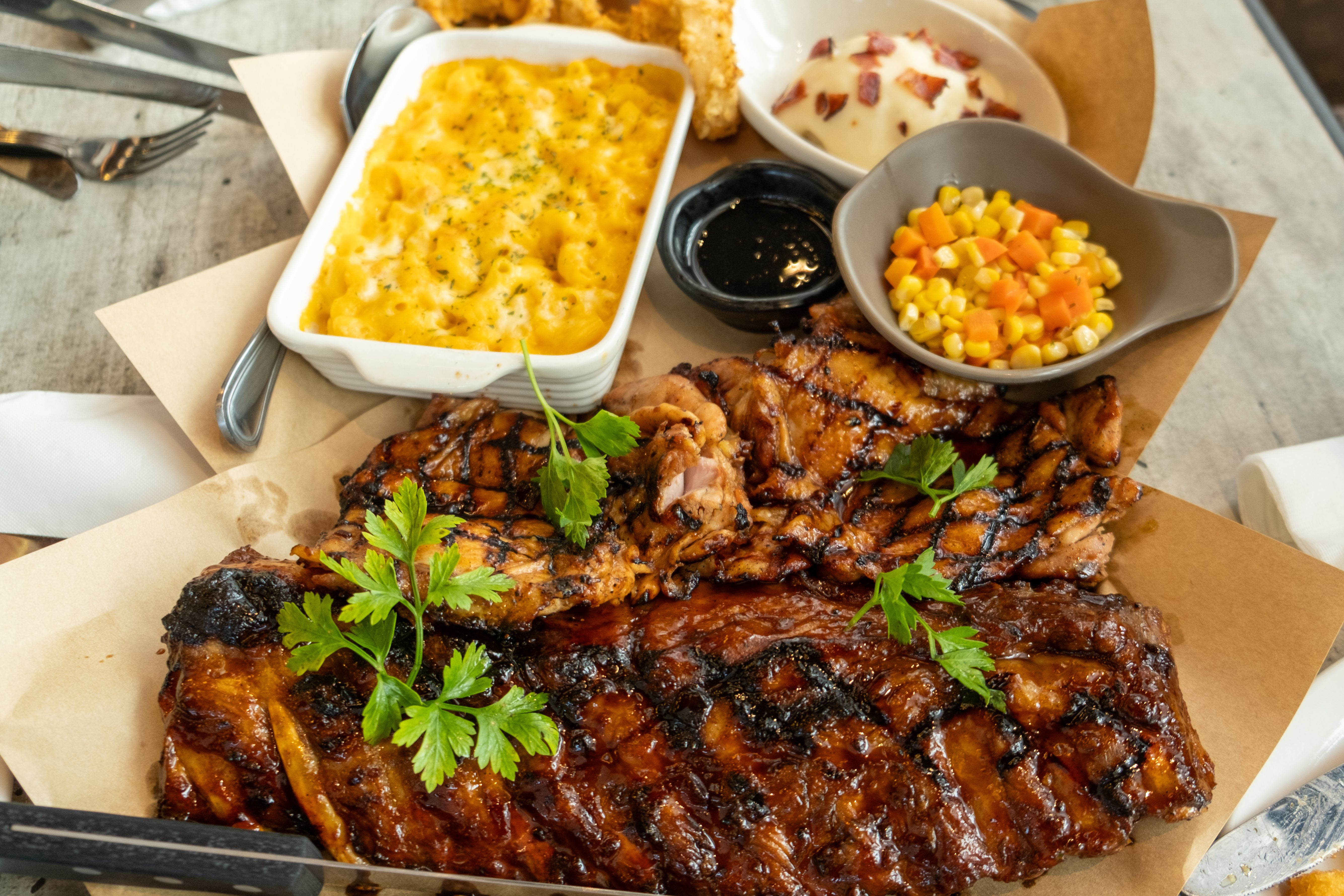 Platter of glazed grilled ribs with mac and cheese, corn salsa and a pot of barbecue sauce