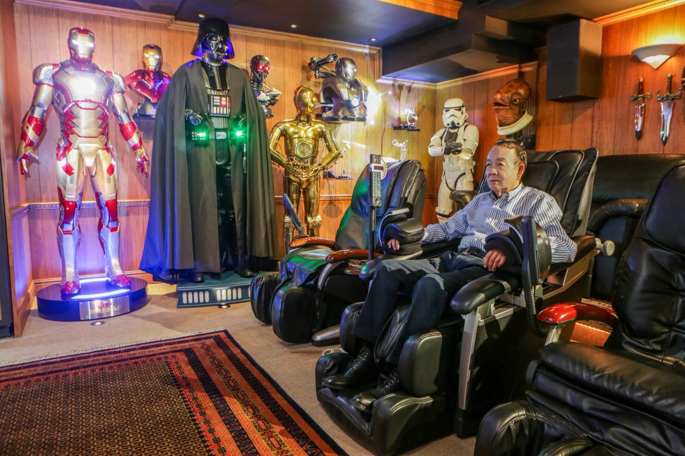 Jun Lopez reclining in a black massage chair in a room lined with life-size Iron Man, Darth Vader, C-3PO and Stormtrooper figures