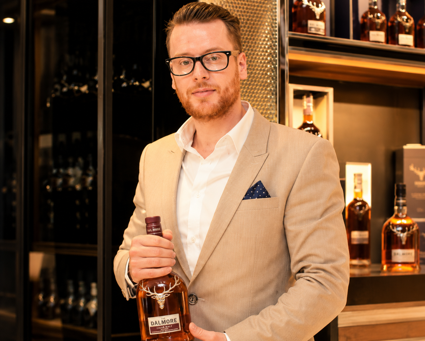 Adam Knox in a tan suit holding a bottle of The Dalmore