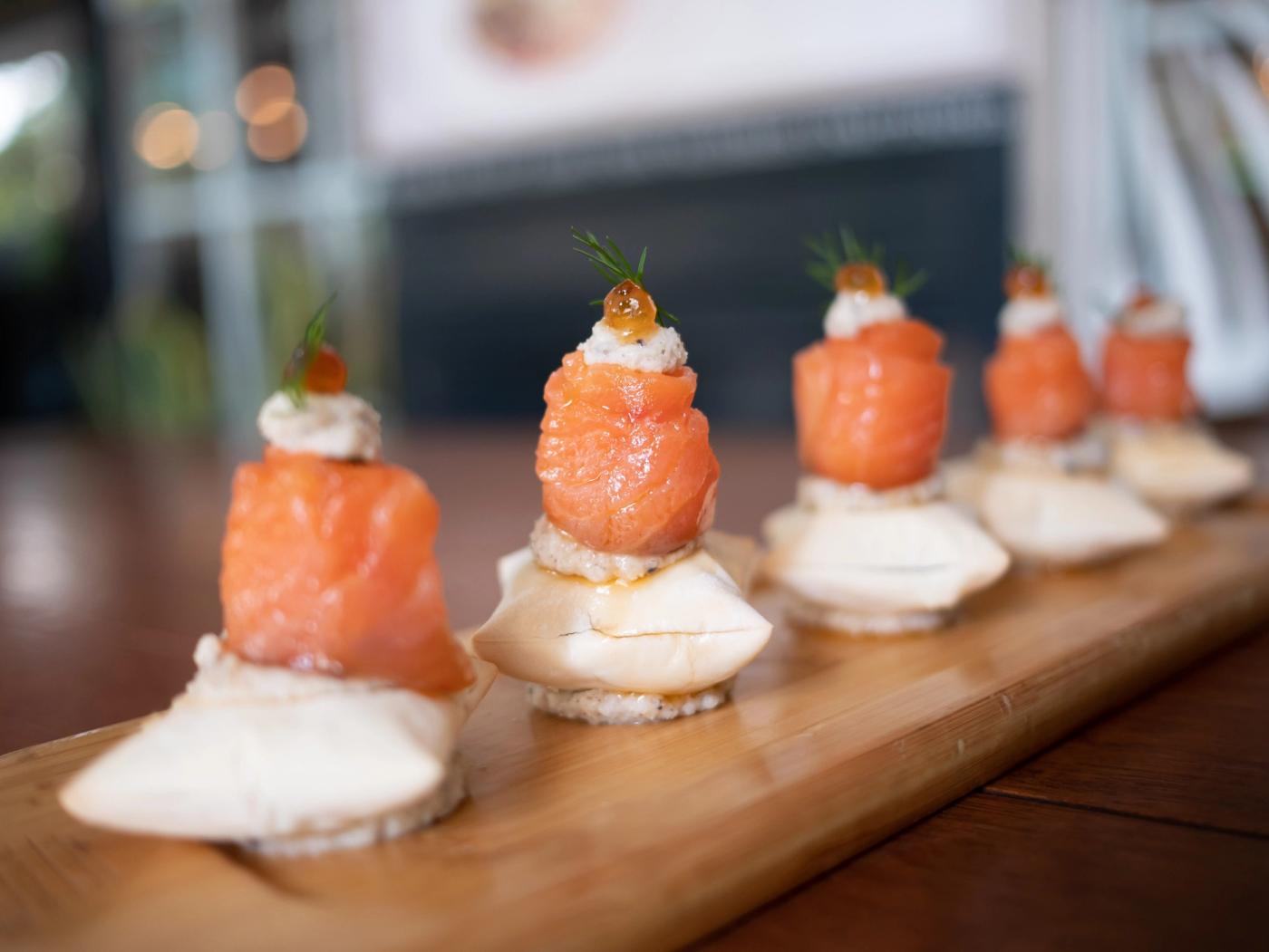 Salmon y Salmón canapés along a wooden board, cured salmon rosettes stacked with cream, roe and dill sprigs
