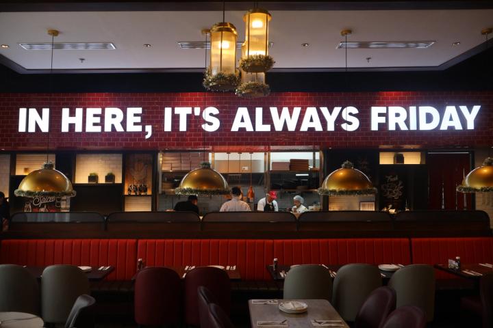 Red banquettes and brass dome lamps beneath a glowing sign reading In here, it’s always Friday