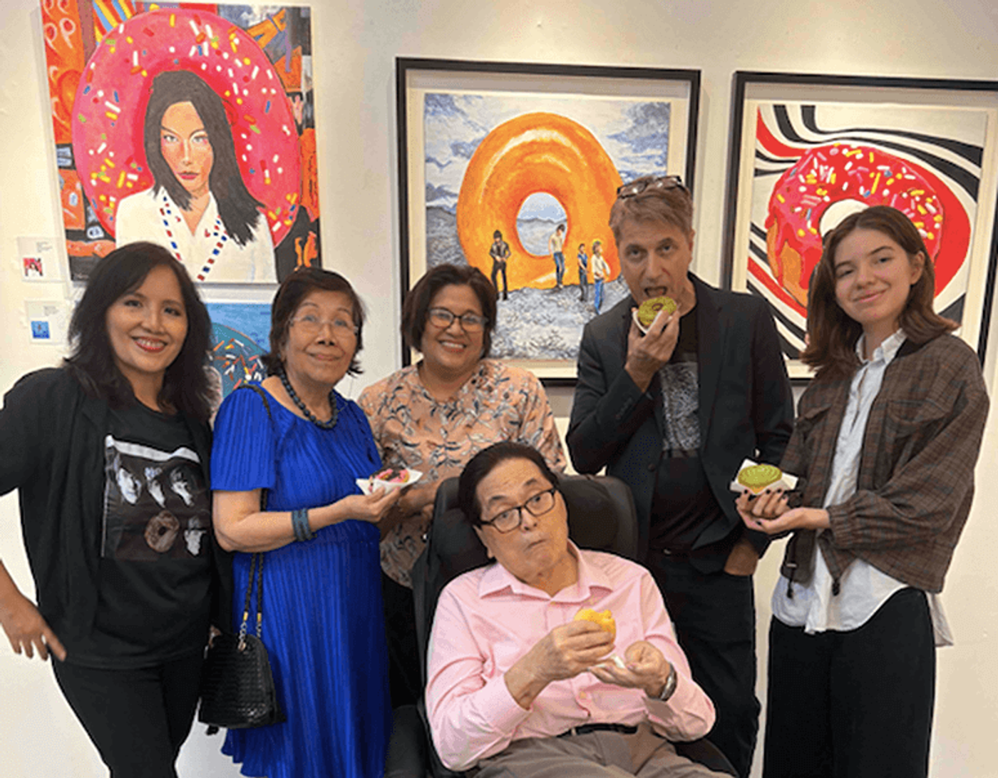 Artist Scott Garceau and family members including Therese Jamora-Garceau and Isobel posing together inside The Crucible Gallery in front of donut-themed paintings