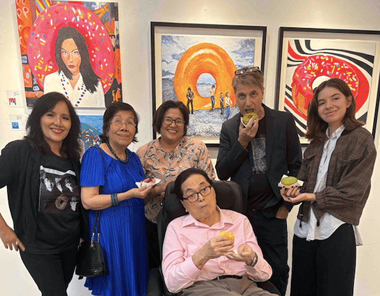 Artist Scott Garceau and family members including Therese Jamora-Garceau and Isobel posing together inside The Crucible Gallery in front of donut-themed paintings