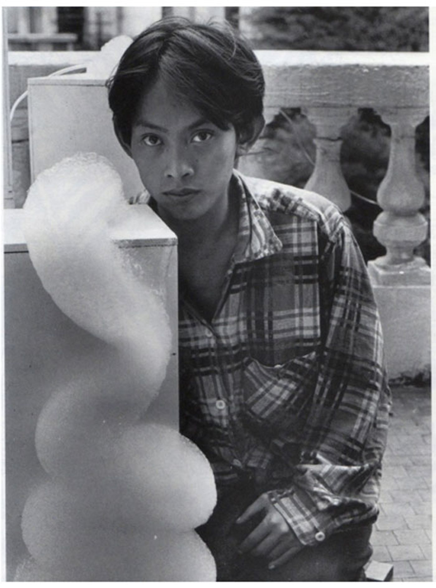 Black and white portrait of a young David Medalla in a plaid shirt beside a column of foam from a bubble machine