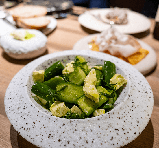 Speckled stone bowl of soured cucumber pieces tossed with herbs and pale creamy cubes
