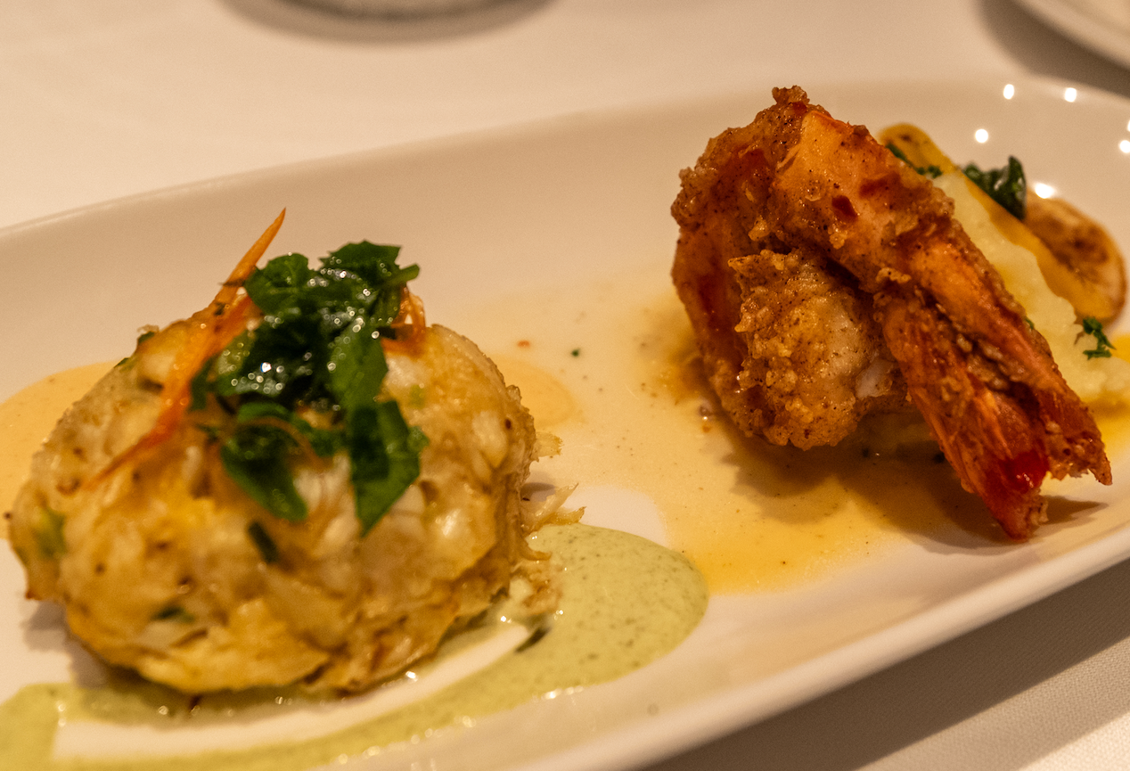 A crab cake topped with herbs beside a crusted fried shrimp over pale sauces at Smith & Wollensky in BGC