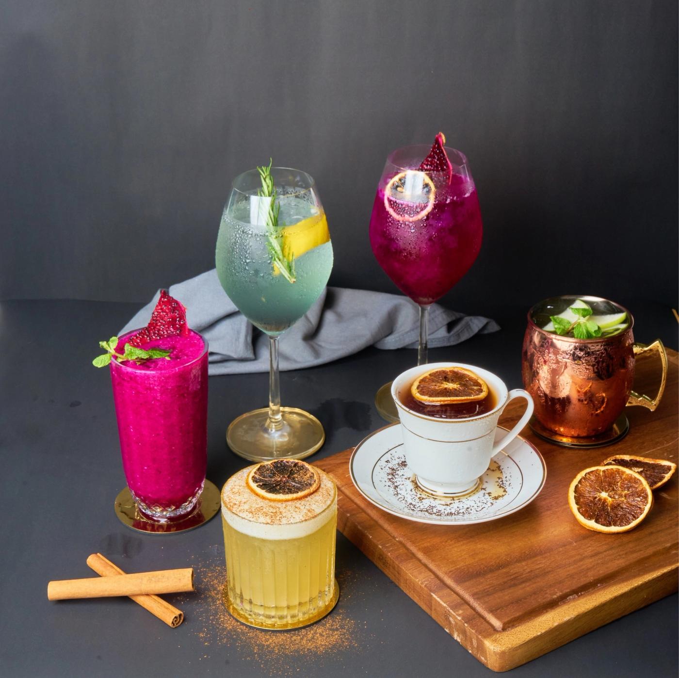 Six colorful craft cocktails at Red Lotus restaurant, including a tall bright purple dragon fruit drink, a turquoise spritz, and a tea-infused cocktail served in a porcelain cup
