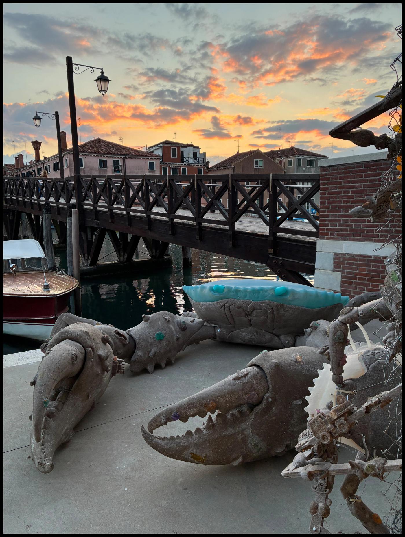 Sculpted crabs with pale shells crawl along a canal-side walkway, a Venetian bridge and lamppost behind