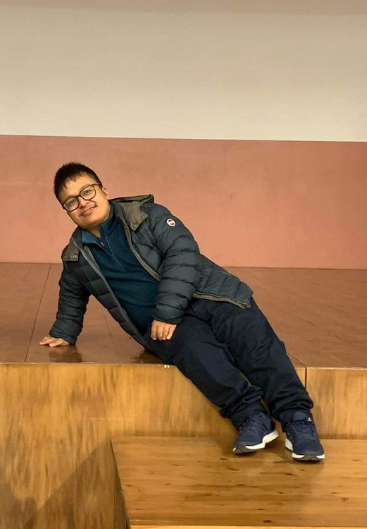 Antonio Lapitan, in glasses and a navy puffer jacket, leans back smiling on a wooden stage platform