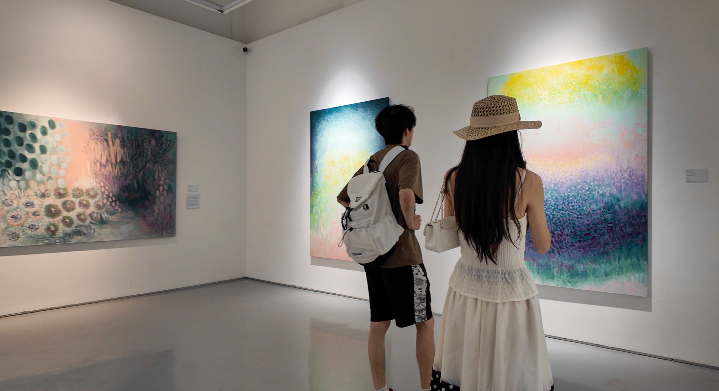 Two visitors, one in a straw hat, viewing Maria Tan’s luminous abstract paintings at The Columns Gallery in Singapore