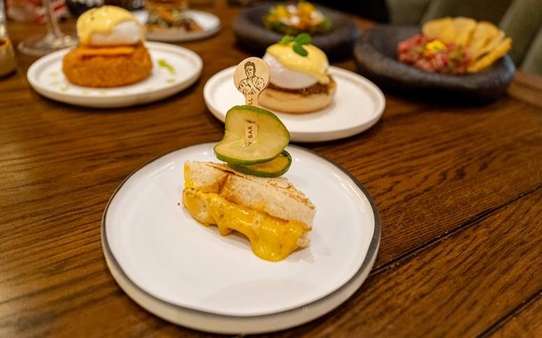 Grilled cheese toastie oozing cheddar, topped with skewered pickles, on a white plate
