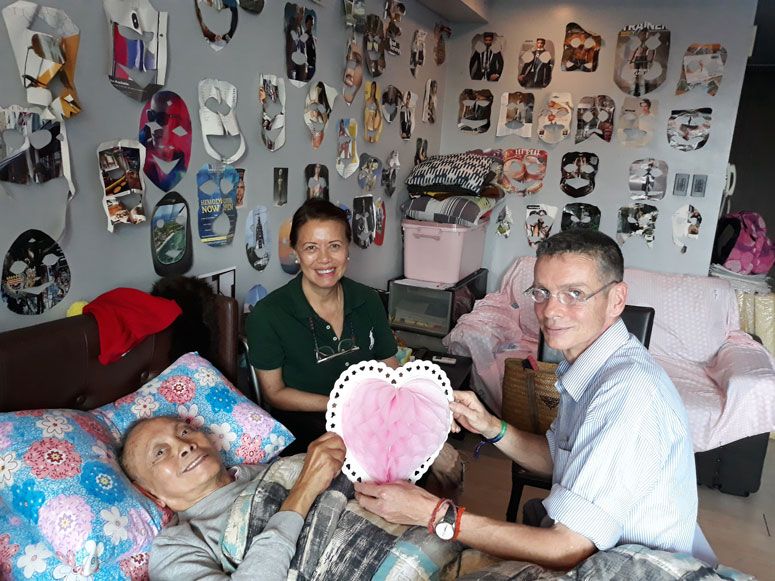 David Medalla in bed beside Petty Benitez-Johannot and Adam Nankervis, a wall of paper cutout artworks behind them