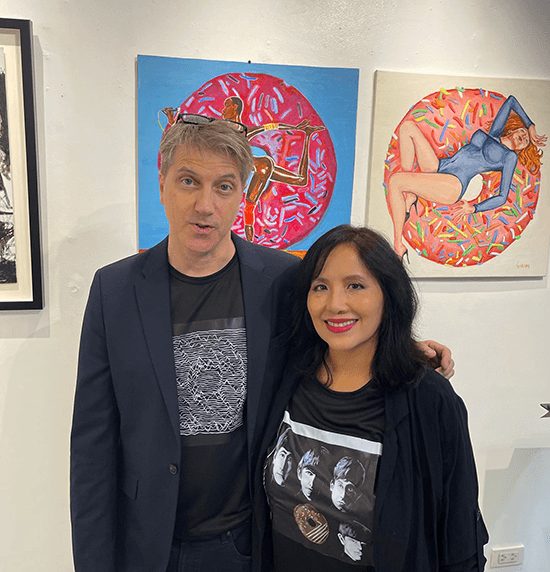 Therese Jamora-Garceau and artist Scott Garceau wearing custom donut-inspired t-shirts and smiling inside the gallery